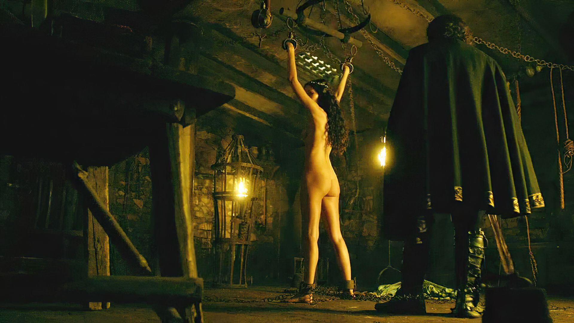 We see Karen Hassan standing naked with her hands chained above her head. 
