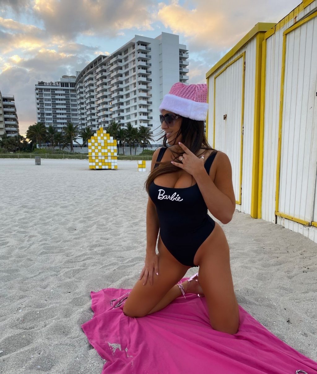 Claudia Romani Poses in a Black Barbie Swimsuit and a Pink Santa Hat (7 Photos)